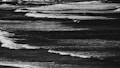 Waves in a body of water move rhythmically toward the shore, creating a serene yet dynamic pattern. The image is monochrome, emphasizing the contrast between the white crests of the waves and the darker water beneath.