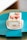 A square layered cake with white cream and strawberries on top, presented on a light pink plate. The cake includes layers of white cream and sponge, with visible strawberry slices inside. It is placed on a teal green surface that contrasts with the cake.