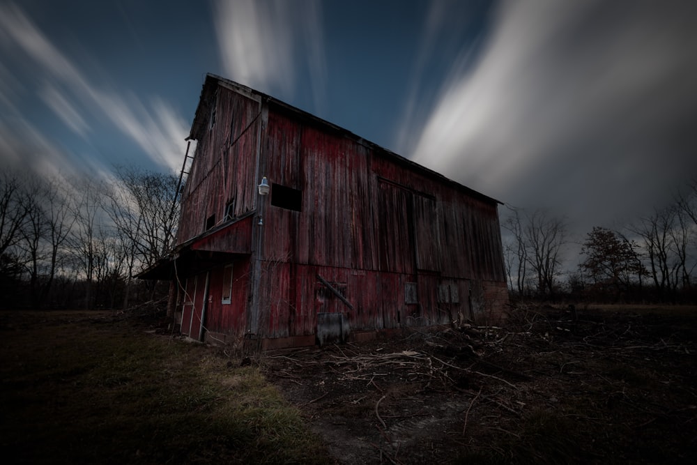 a red barn in a field under a cloudy sky