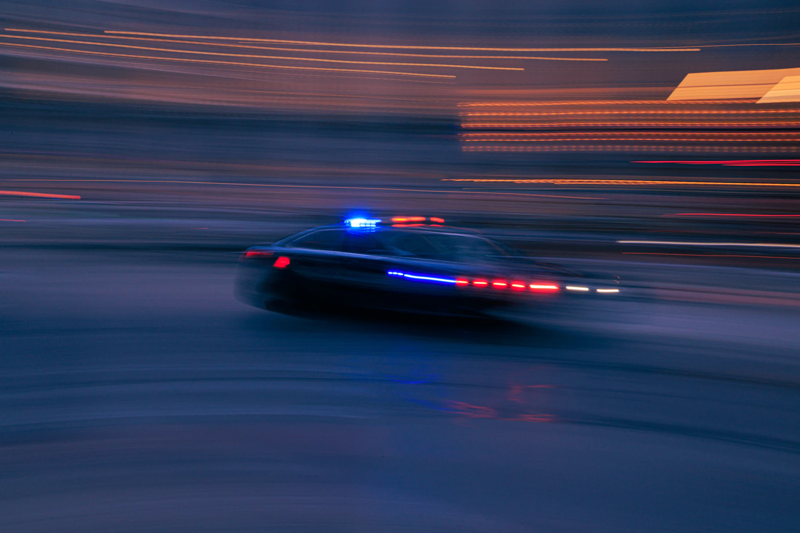 A police car with its lights on, driving down a street at night.
