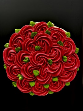 An intricately designed cake with a floral pattern, featuring a series of red rose-like shapes made from frosting, interspersed with small, bright green leaf decorations. The black background enhances the vividness of the colors.