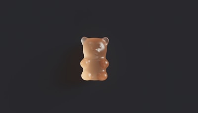 Hand holding a single gummy with a blurred modern background in black and gold tones.