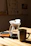 A close-up of a steaming cup of pour-over coffee on a wooden table bathed in soft morning light.