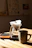 A close-up of a steaming cup of pour-over coffee on a wooden table bathed in soft morning light.