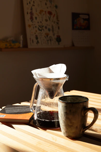 A cozy kitchen corner with a steaming cup of coffee next to a vintage pour-over set, sunlight streaming through a nearby window.