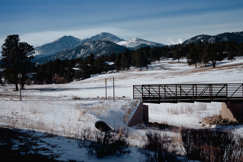 a bridge over a snow covered field with mountains in the background
