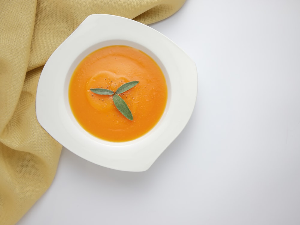 a bowl of carrot soup with a sprig of sage