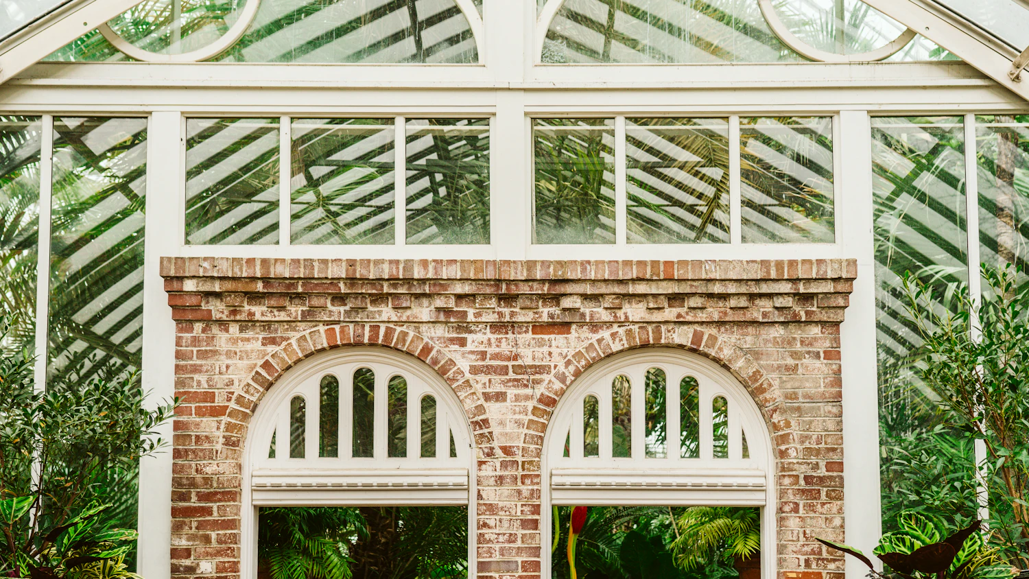 A brick-based Victorian glasshouse with arched windows, half hidden by green leaves