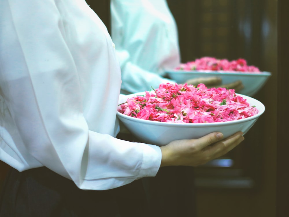 a person holding a bowl of pink flowers