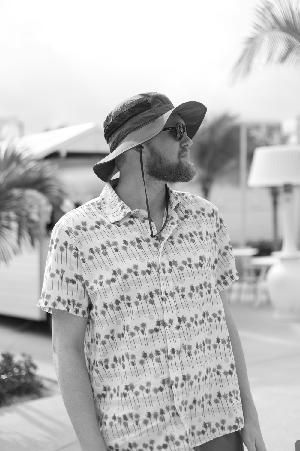 a man wearing a hat and sunglasses standing on a sidewalk