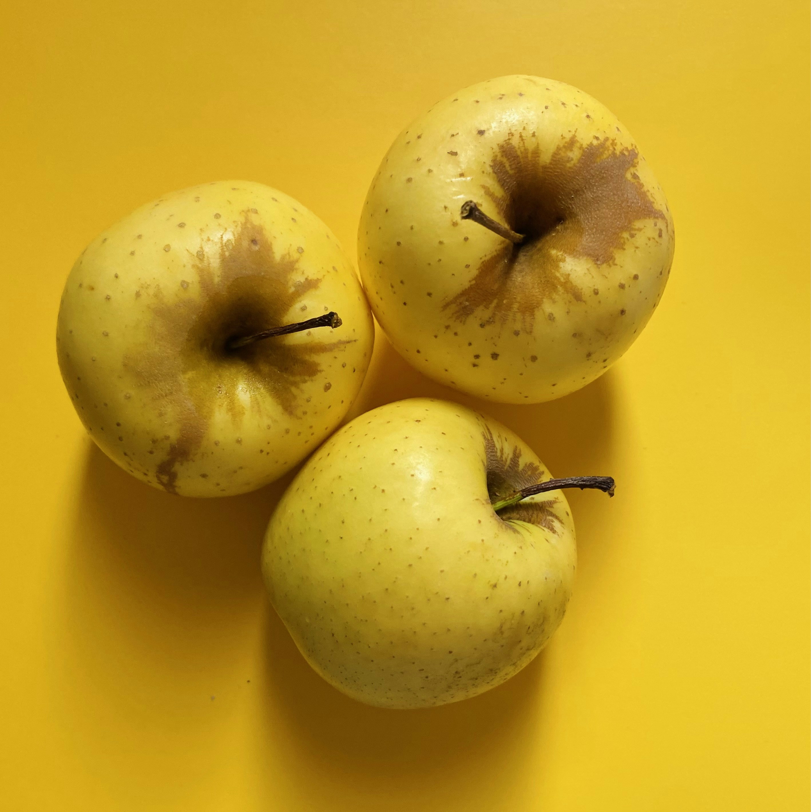 three apples sitting on top of a yellow surface