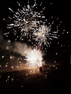 A vibrant display of fireworks illuminating the night sky, with bursts of light and sparks radiating in multiple directions. The glowing effects create a dynamic and energetic visual spectacle against the dark background.