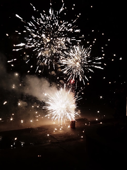 A vibrant display of fireworks illuminating the night sky, with bursts of light and sparks radiating in multiple directions. The glowing effects create a dynamic and energetic visual spectacle against the dark background.