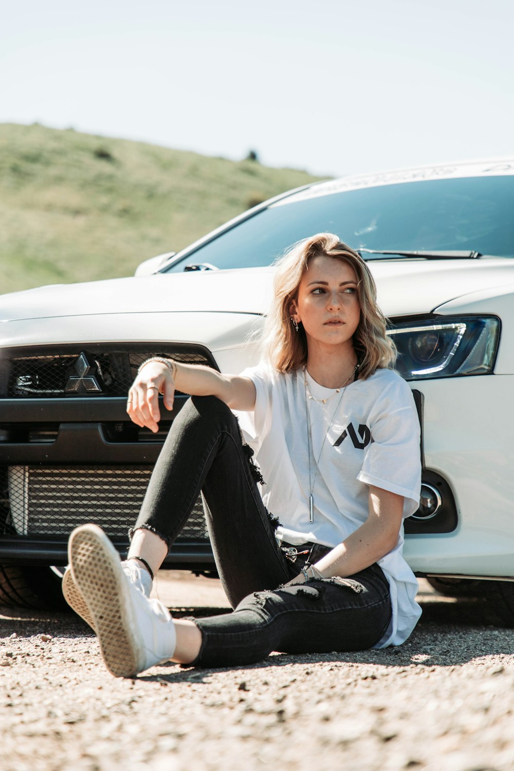 a woman sitting on the ground next to a white car