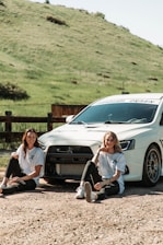 A happy couple enjoying a scenic tour in Armenia, standing next to a sleek rental car with rolling hills in the background.