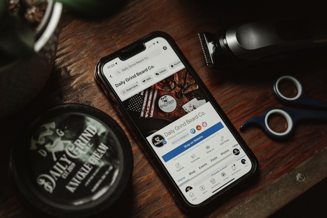 a cell phone sitting on top of a wooden table, Product photo of Knuckle Cream Beard Balm and social media for Daily Grin