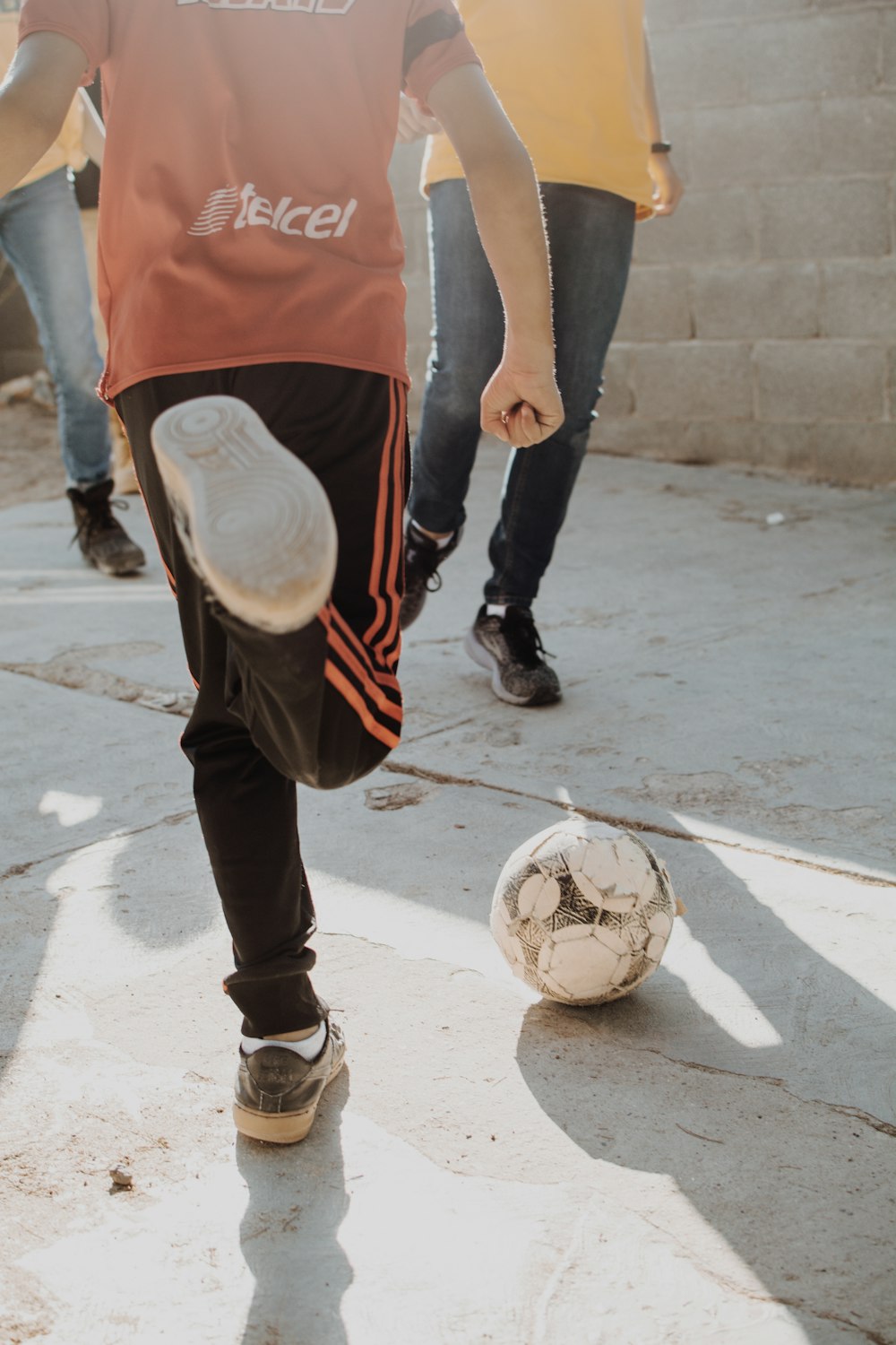 a young boy kicking a soccer ball on a sidewalk