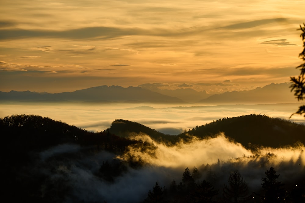 the sun is setting over the mountains and fog