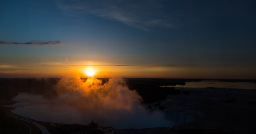 the sun is setting over a steaming geyser