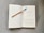 An open book rests on a textured gray surface. A pencil with a blue eraser lays diagonally across one of the pages. The book's content includes a title, 'Murder by Design: The Psychology of Bloodlust,' and a passage discussing topics related to killing and survival.
