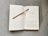 An open book rests on a textured gray surface. A pencil with a blue eraser lays diagonally across one of the pages. The book's content includes a title, 'Murder by Design: The Psychology of Bloodlust,' and a passage discussing topics related to killing and survival.