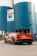 A sleek, red sports car is parked in front of a large industrial building with blue and white silos. An American flag and a sign for Mountain Cement Company are visible on the building.