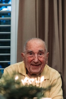 A smiling home care nurse assisting a senior gentleman with his morning routine surrounded by bright yellow and green decor.