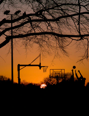 A sunset silhouette of young athletes shooting hoops together, embodying teamwork and hope.
