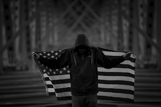 A patriotic-themed hoodie displayed on a mannequin with a backdrop of waving American flags