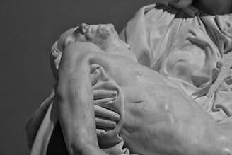 A detailed sculpture of a reclining figure with a serene expression, showcasing intricate drapery and muscular details. The sculpture is made of marble, highlighting the craftsmanship and realistic depiction of the human form.