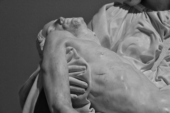 A detailed sculpture of a reclining figure with a serene expression, showcasing intricate drapery and muscular details. The sculpture is made of marble, highlighting the craftsmanship and realistic depiction of the human form.