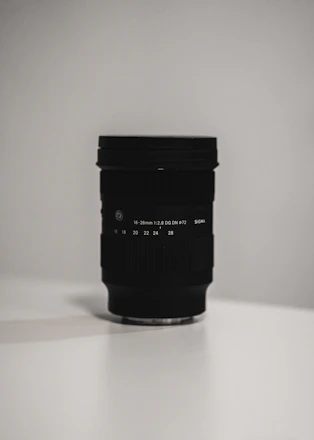 A sleek camera lens resting on a minimalist black surface with soft natural light highlighting its details.