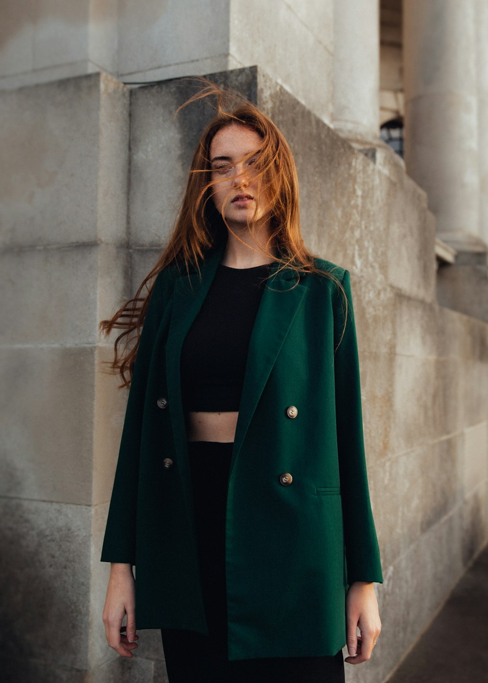 a woman standing next to a wall wearing a green coat