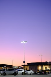 A modern parking lot with clear signage and cars parked neatly under bright lights at dusk.