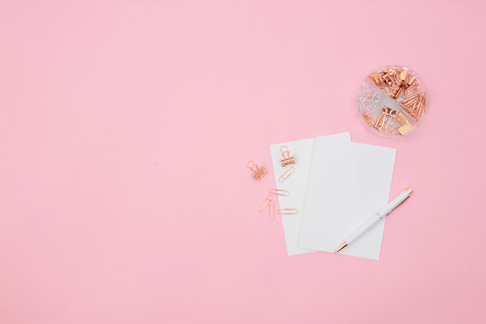 a pink background with a notepad, pen, and a pair of scissors