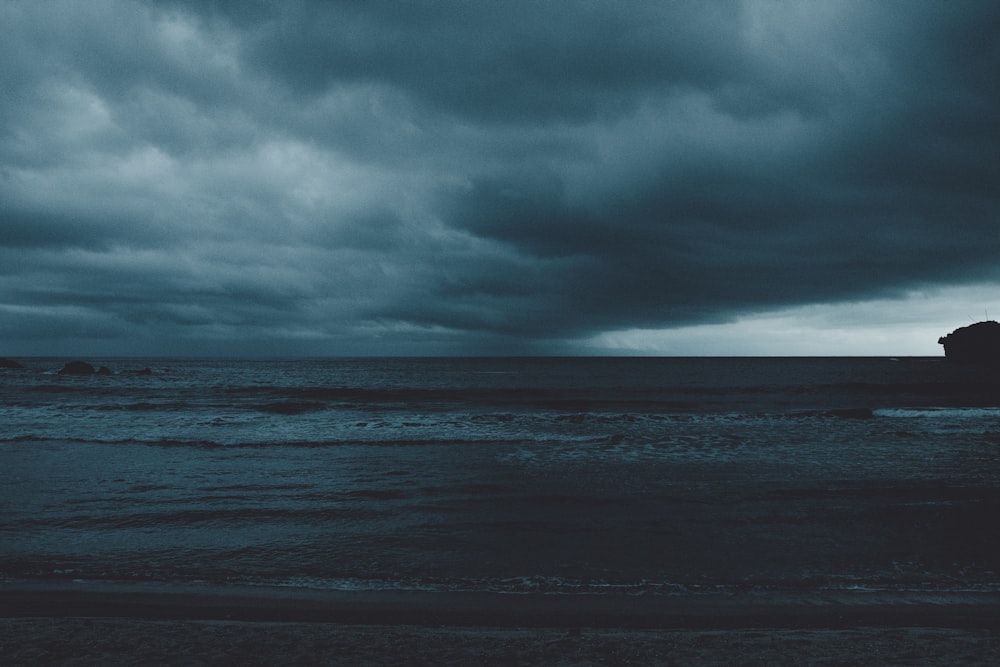 a black and white photo of the ocean under a cloudy sky