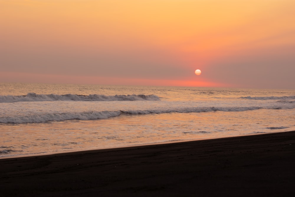 the sun is setting over the ocean on the beach