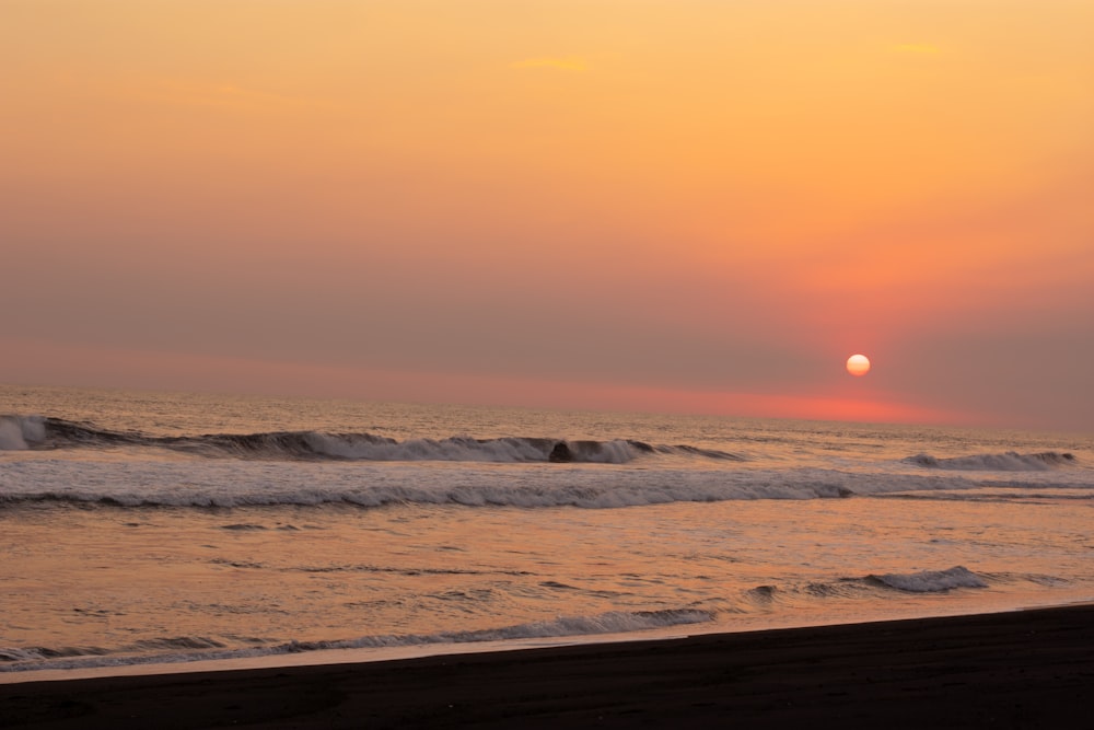 the sun is setting over the ocean on the beach