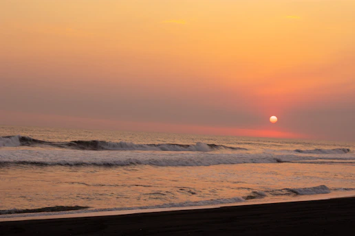 A vibrant oil painting of a serene seascape at sunset, with waves gently rolling onto a sandy shore.