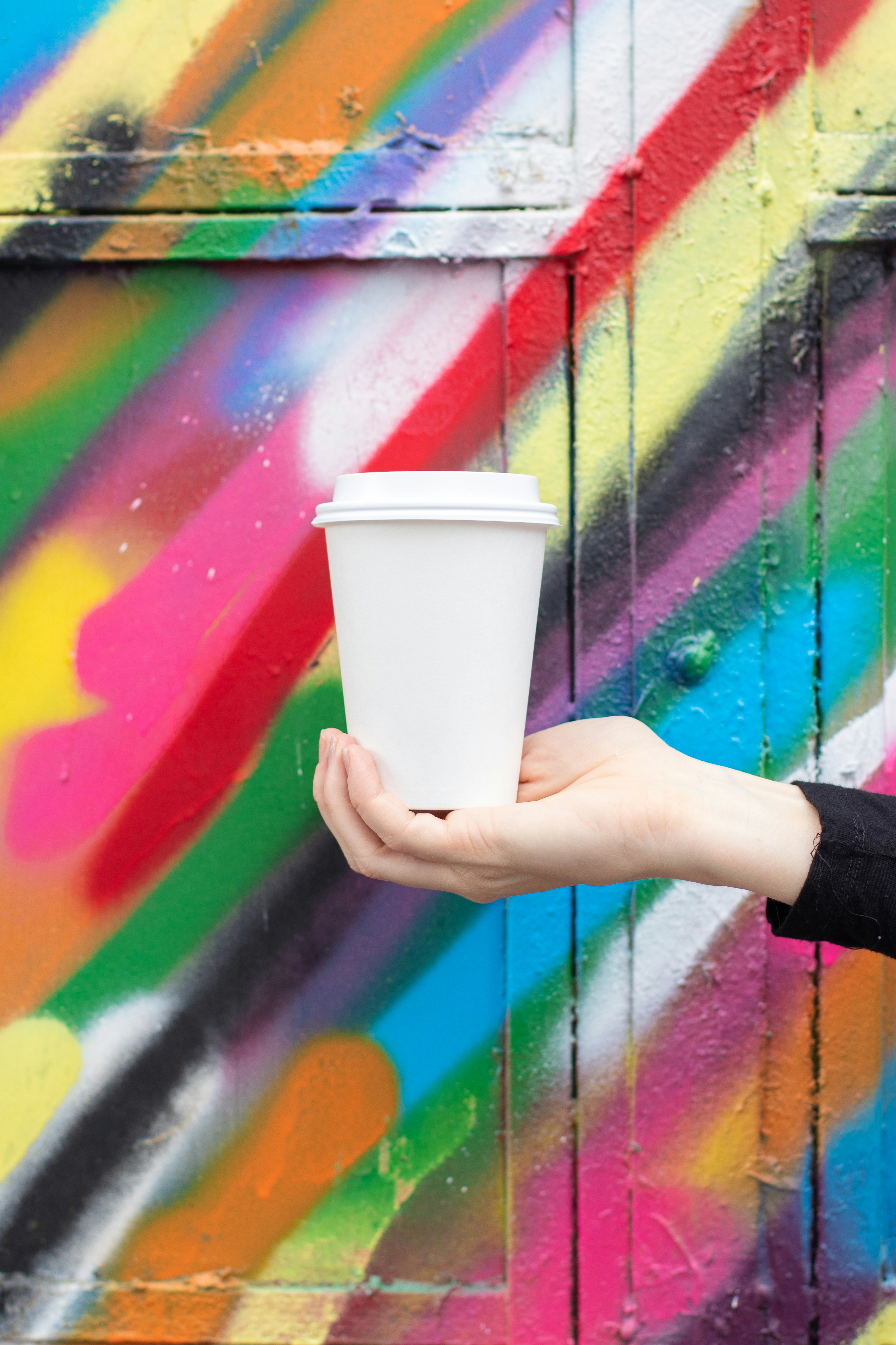 Une personne tenant une tasse de café devant un mur coloré