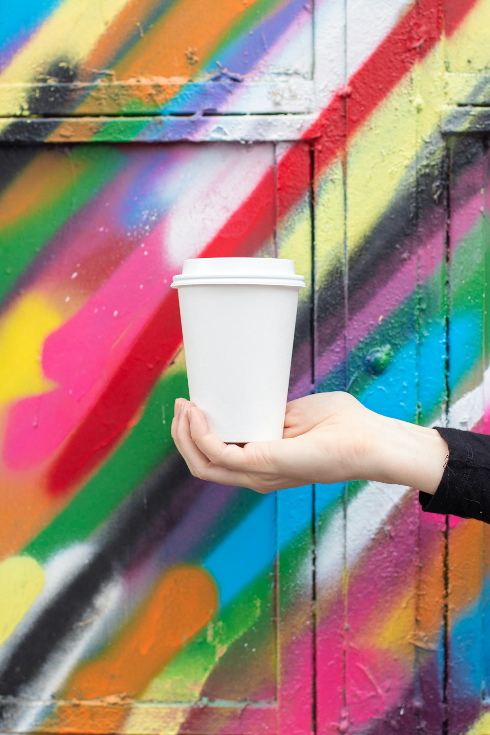 a person holding a cup of coffee in front of a colorful wall