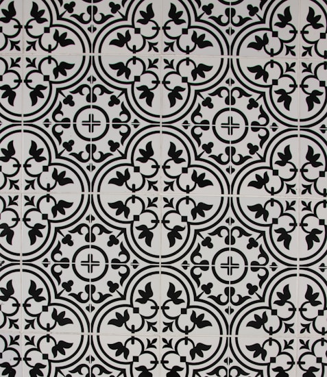 A series of intricately designed black and white tiles form a repeating pattern featuring symmetrical curves and floral motifs. The pattern appears to be both geometric and organic, creating a vintage or classic aesthetic.