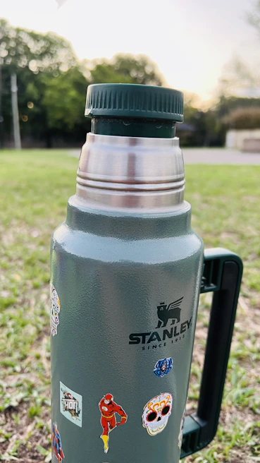 A hand holding a custom printed thermos with bright geometric patterns outdoors