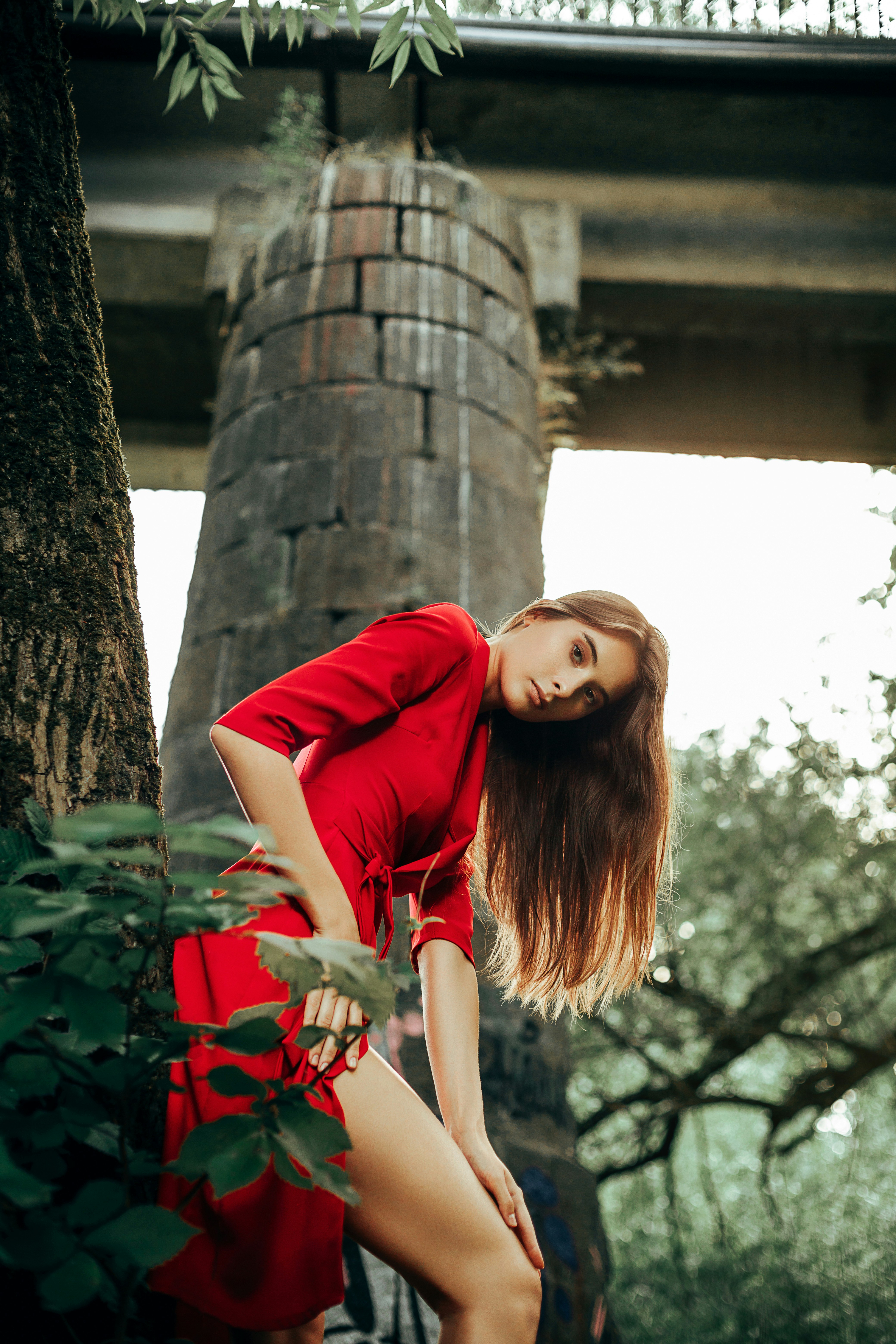 a woman in a red dress leaning against a tree