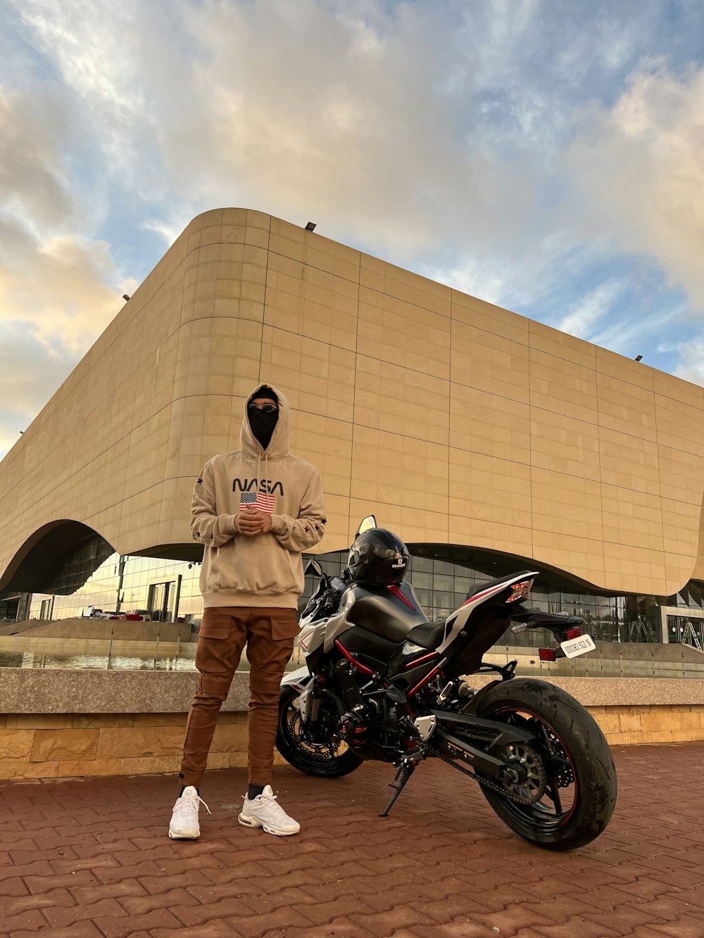 Un hombre parado junto a una motocicleta frente a un edificio