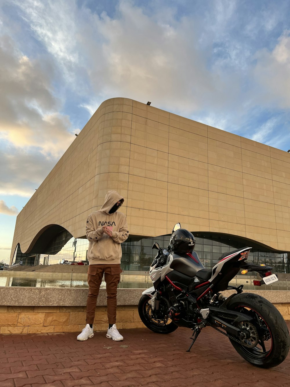 Un homme debout à côté d’une moto devant un immeuble