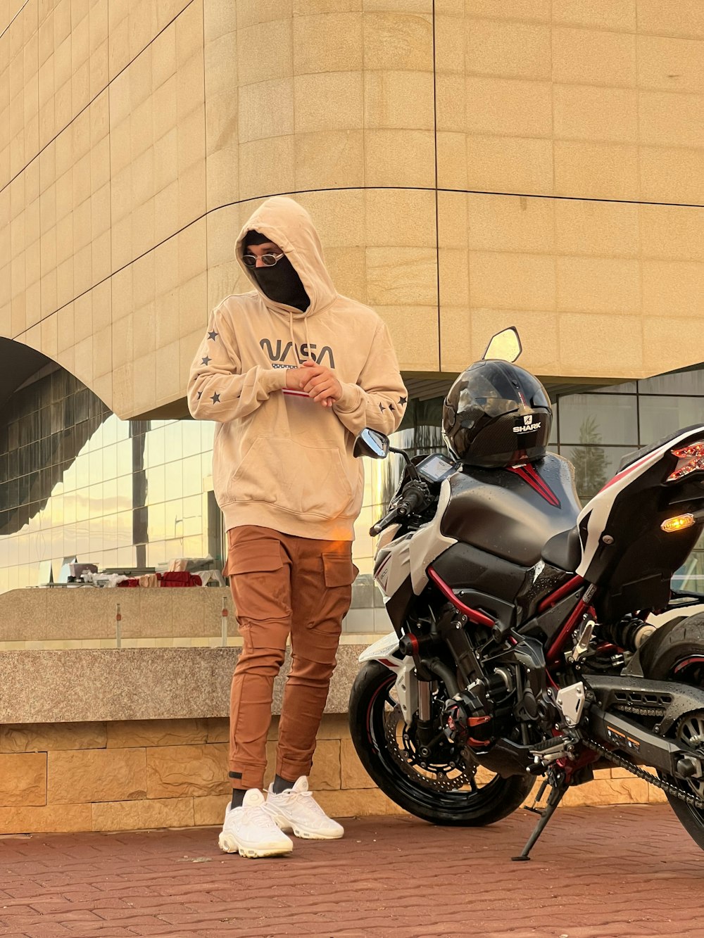 a man in a hoodie standing next to a motorcycle