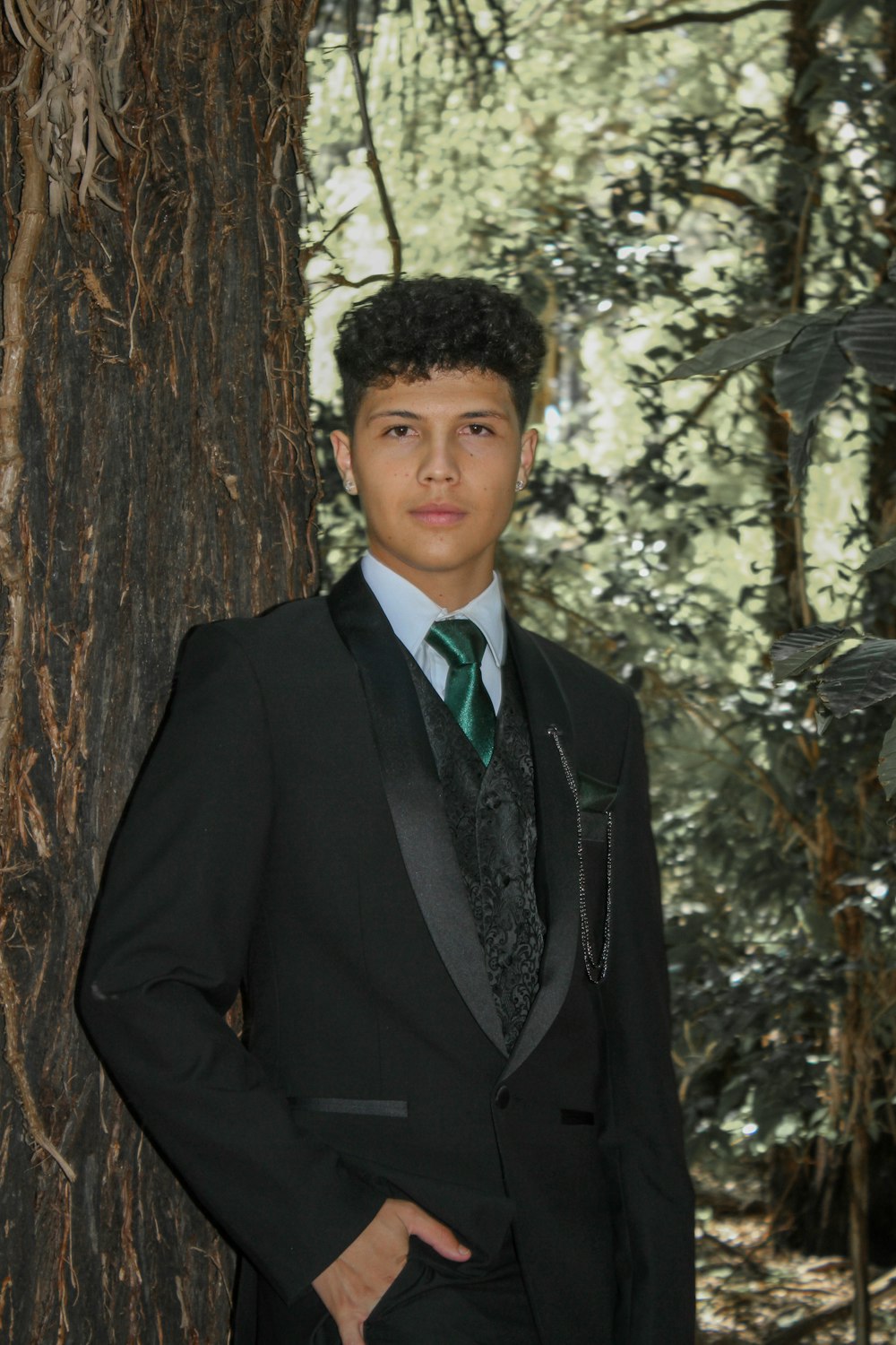 a young man in a suit standing next to a tree