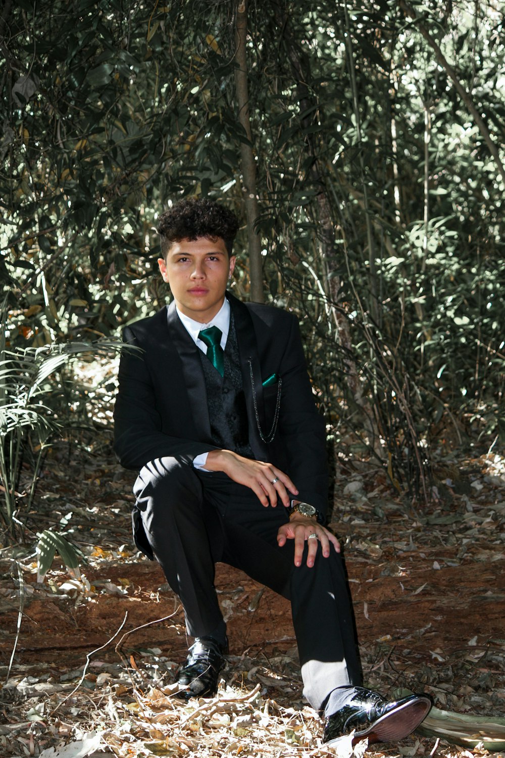 a young man in a suit sitting in the woods