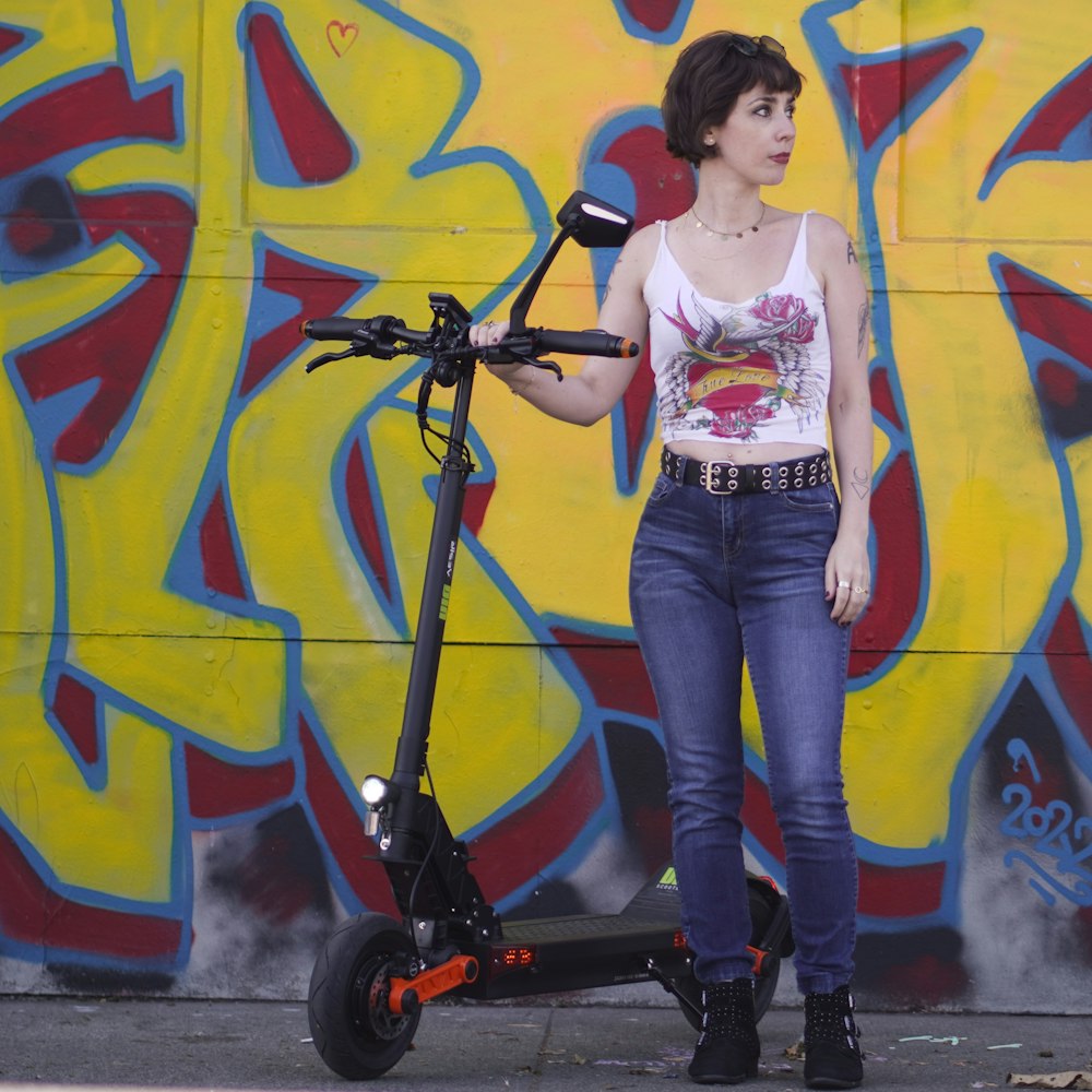 a woman standing next to a scooter in front of a wall with graffiti